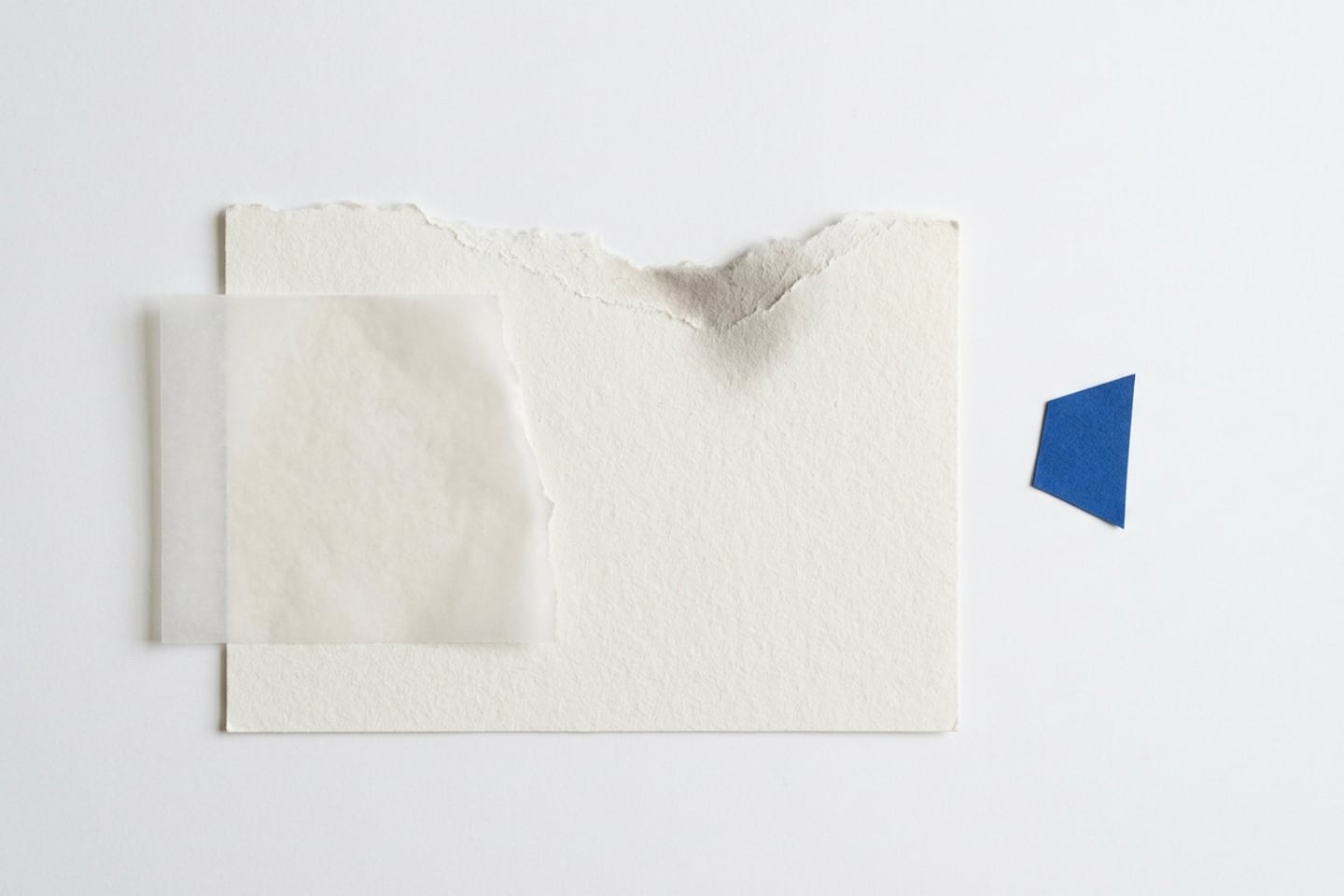 Draufsicht auf eine Papiercollage: Eine gerissene Kante mit feinem Faserbart, überlagert von Transparentpapier und einem blauen Reststück.